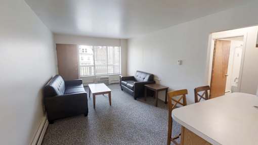 A living room with a black couch, a black chair, a white table, and a brown chair.
