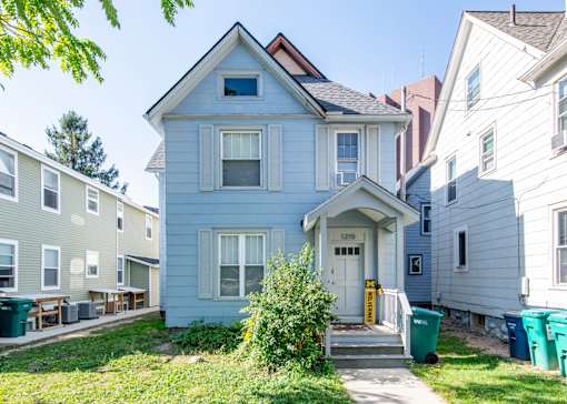 A blue house with a white door and windows is in front of other houses.