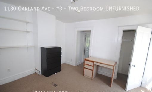 A room with a black dresser and a wooden desk in it.