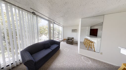 A living room with a couch, a chair, and a small kitchenette.