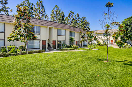A grassy area in front of a building with trees and bushes.