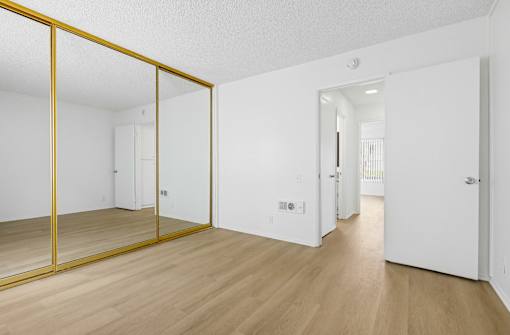 A room with a white door and a white wall with a mirror on the left side.