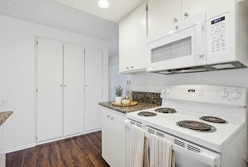 A white kitchen with a stove, microwave, and cabinets.