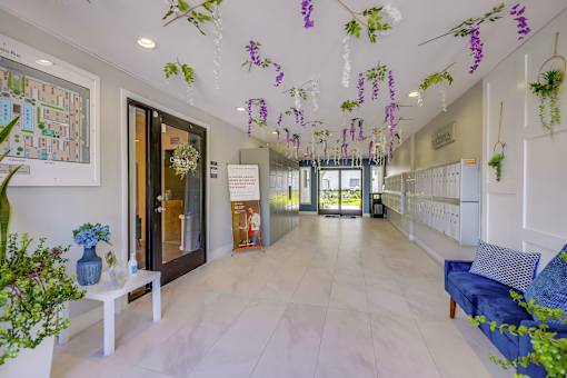 A hallway with a blue sofa and purple flowers hanging from the ceiling.