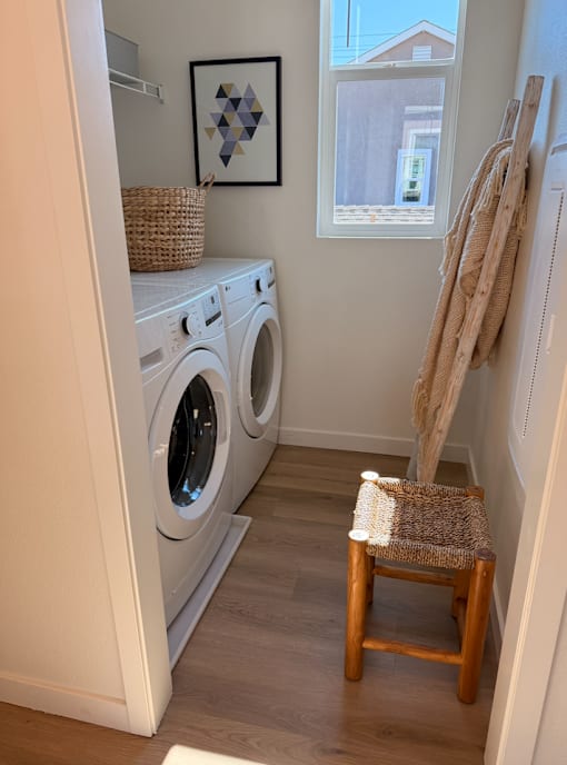 A small laundry room with a chair and a basket on top of the washing machine.