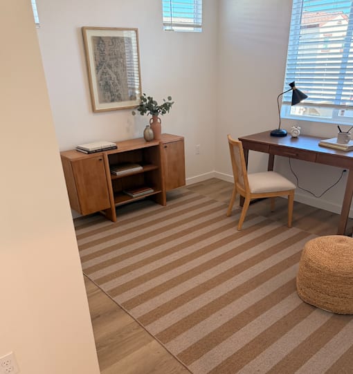 A room with a desk, chair, and a cabinet with a vase on top.