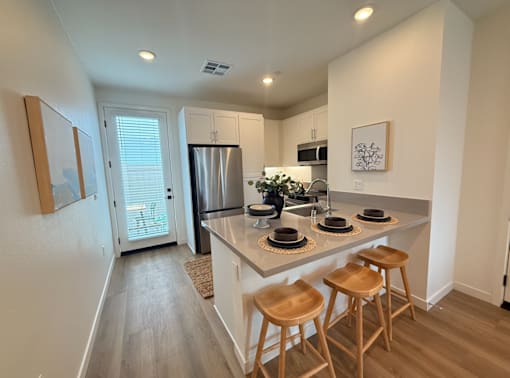A kitchen with a refrigerator, microwave, and two bar stools.