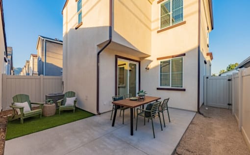 A patio with a table and chairs is in front of a house.