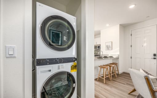 A modern laundry room with a washing machine and a view into a kitchen.