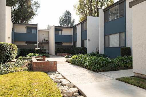 A brick planter sits in the middle of a grassy area in front of apartment buildings.