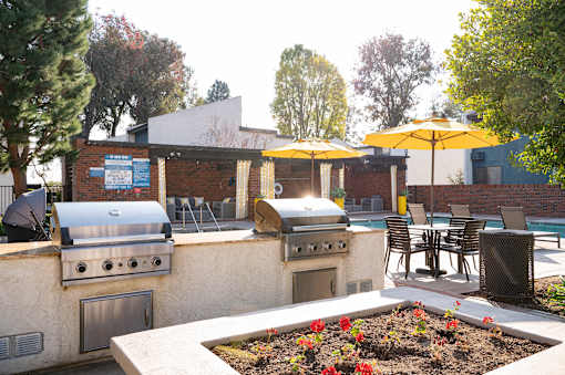 A patio with a grill and chairs under yellow umbrellas.