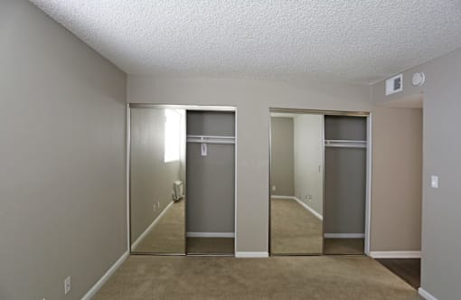 A room with a carpeted floor and two closets with mirrors.