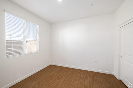 A room with a wooden floor and a window with blinds.