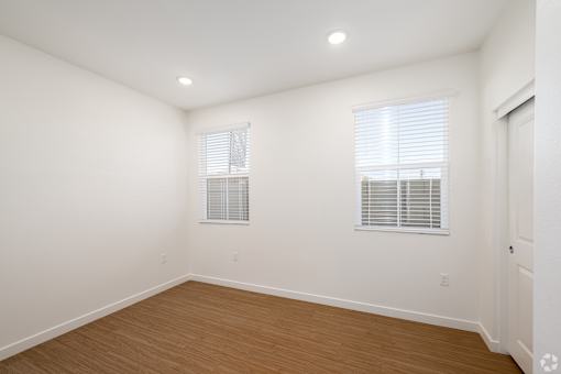 A room with wooden floors and two windows with blinds.
