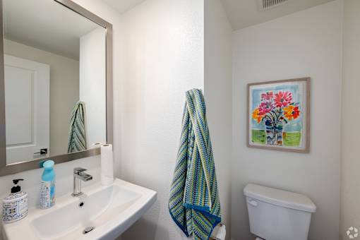 A bathroom with a white toilet, a white sink, a mirror, and a picture of flowers on the wall.