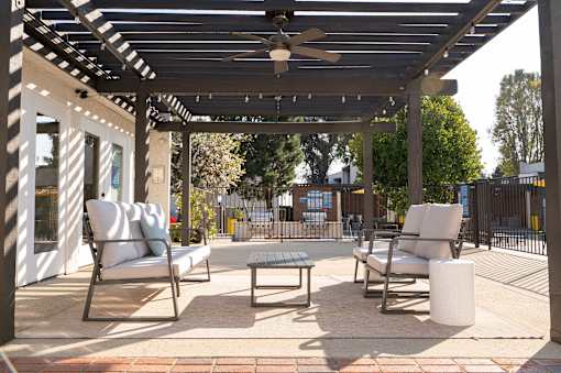 A patio with a white couch, two chairs, and a table under a pergola.