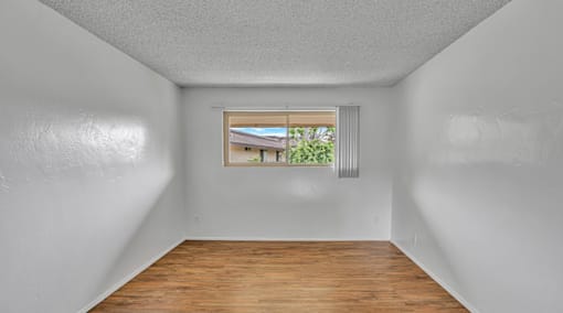 A room with a window showing a view of a house and greenery outside.