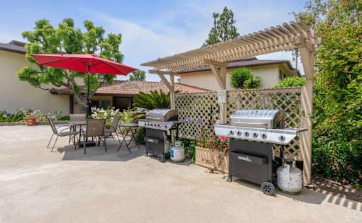 A patio with a grill and a table under a red umbrella.