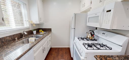 A white kitchen with a stove, sink, and cabinets.