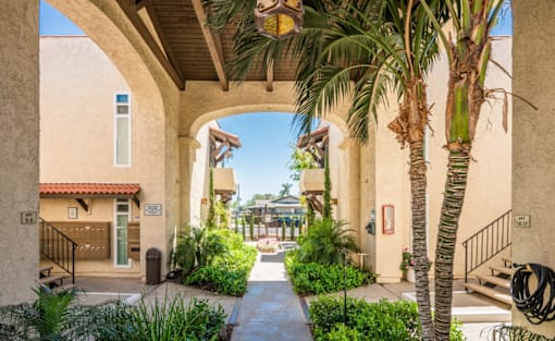 A pathway leads through a courtyard with a palm tree and a building with a red tile roof.