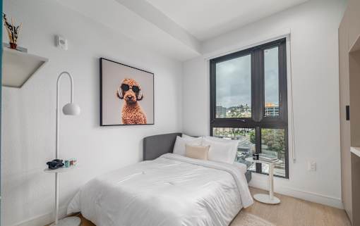 A bedroom with a bed, a lamp, and a picture of a dog on the wall.