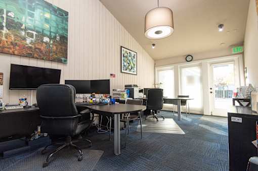 A room with a desk, chairs and a painting on the wall.