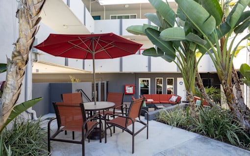 A patio with a table and chairs under a red umbrella.