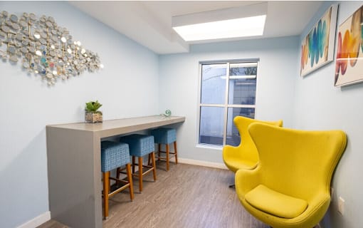 A yellow chair is in front of a grey desk with a plant on it.