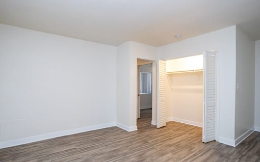 A room with white walls and wooden flooring with a doorway leading to another room.