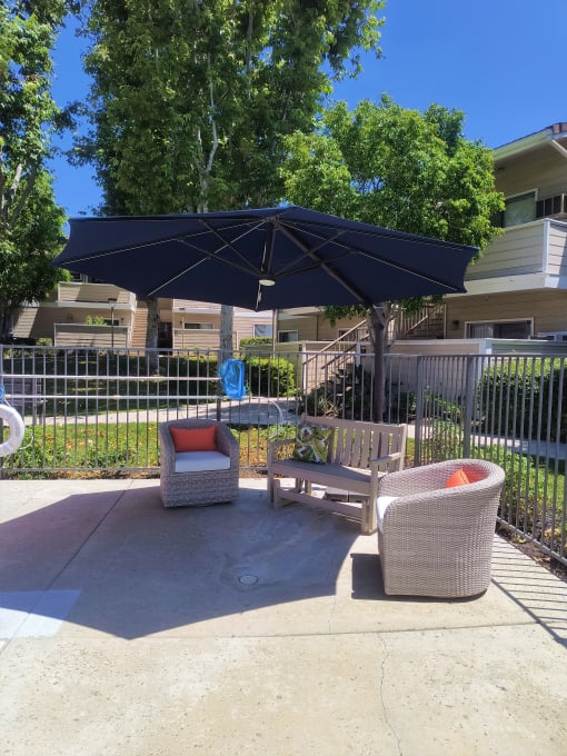 a patio with two chairs and an umbrella in front of a fence