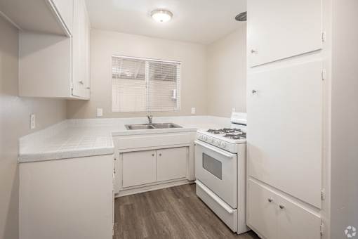 A white kitchen with a stove, sink, and cabinets.
