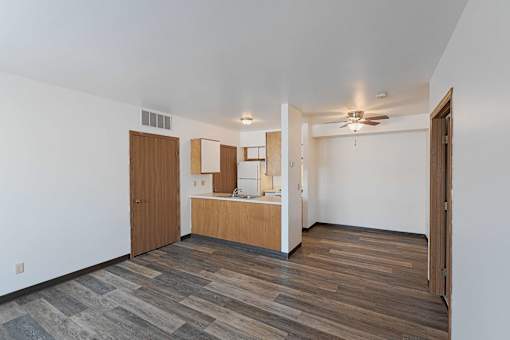 an empty living room with a kitchen and a ceiling fan