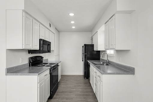 A black refrigerator sits in a kitchen with white cabinets.