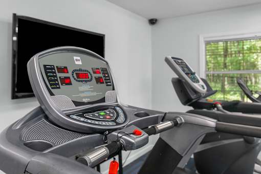 A treadmill with a digital display and control panel is in a room with a window.