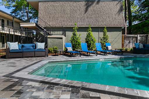 A pool with a tiled floor and a patio with chairs and a table.