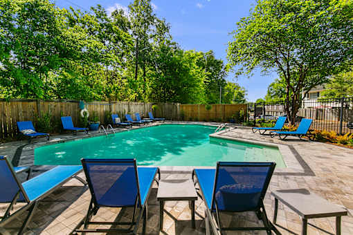 A pool surrounded by blue chairs and trees.