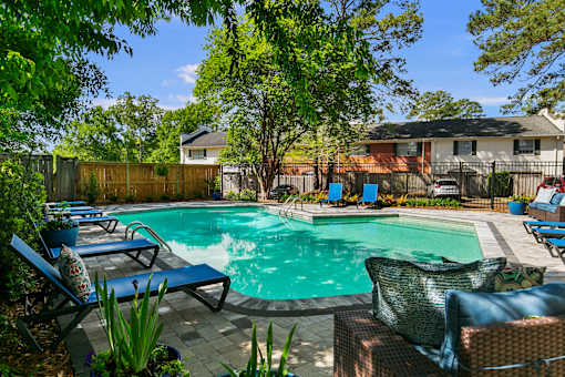 A pool surrounded by trees and chairs.