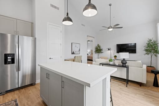 a white kitchen with a large island and a stainless steel refrigerator at Village of Chandler Apartments, Chandler