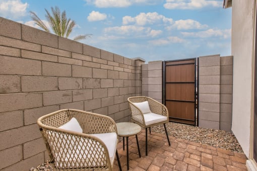 a patio with two chairs and a table next to a brick wall at Village of Chandler Apartments, Chandler, AZ, 85249