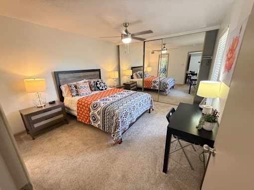 A bedroom with a bed, desk, and mirror.