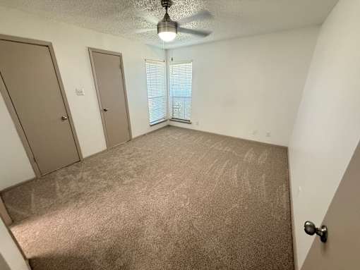 A room with a carpeted floor and a ceiling fan.