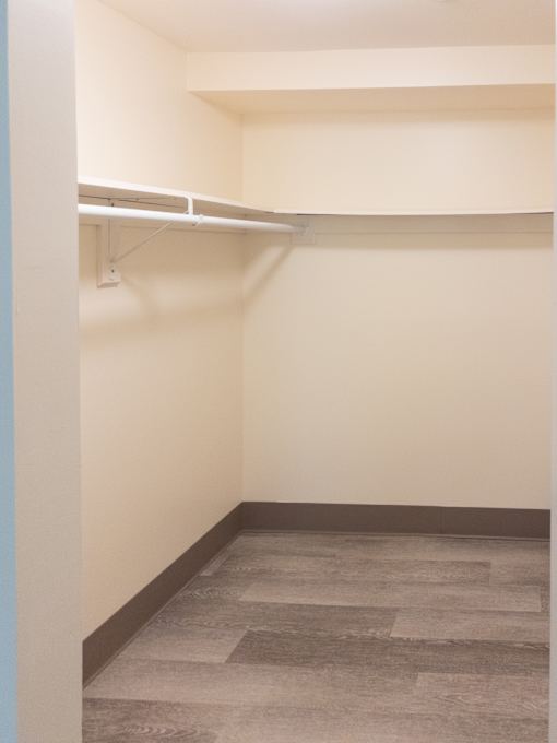A walk in closet with a shelf and a grey floor.