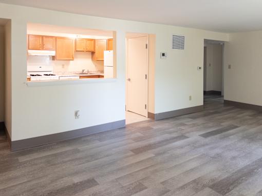 A kitchen with wooden cabinets and a countertop is visible through a window in a room with wooden flooring.