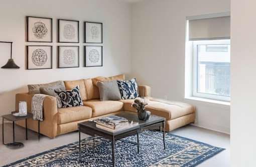 A living room with a tan couch, a coffee table, and a blue rug.