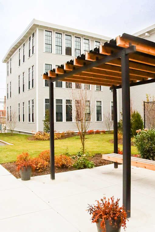 A bench under a pergola with a white building behind it