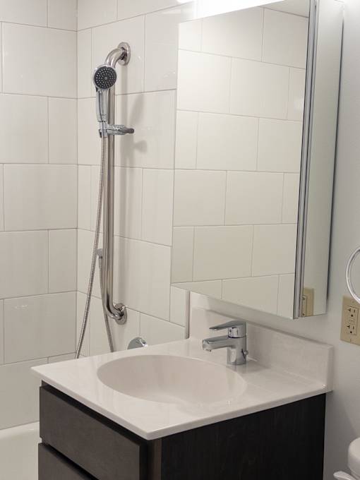 A white sink in a bathroom with a shower head and mirror.