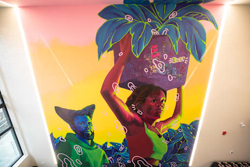 A woman is carrying a large pineapple on her shoulder.