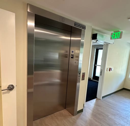 a stainless steel elevator in a hallway with a exit sign