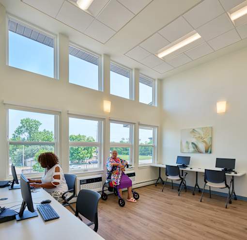 A woman is sitting at a desk in a room with large windows.