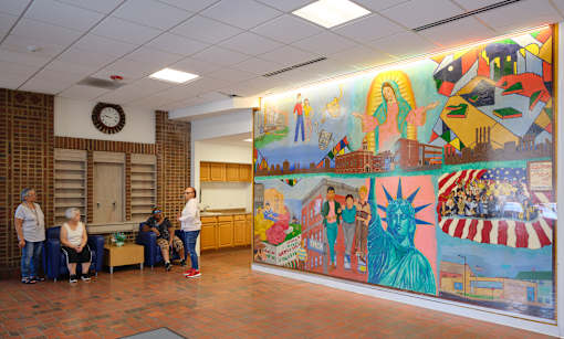 A group of people are sitting and standing in a room with a large mural on the wall.